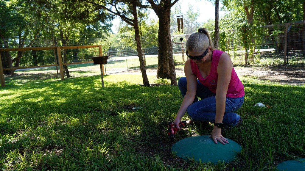 A woman uses a drill to open a septic tank lid.